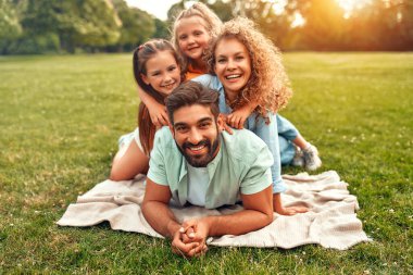 Mutlu, genç bir aile babası, anne ve iki kızı güneşli bir günde parkta çimlerin üzerinde uzanıyor, birlikte eğleniyor ve tatil günlerinde dinleniyorlar..