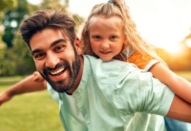 Mutlu bir genç baba kızıyla oynuyor, onu sırt üstü yuvarlıyor, sıcak bir hafta sonu gününde parktaki çayırda koşuyor ve eğleniyor..