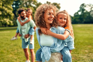 Mutlu bir aile babası, anne ve iki kızı sıcak güneşli bir günde parkta çayırlarda oynuyorlar, birlikte eğleniyorlar ve izin günlerinde dinleniyorlar..