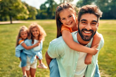 Mutlu bir aile babası, anne ve iki kızı sıcak güneşli bir günde parkta çayırlarda oynuyorlar, birlikte eğleniyorlar ve izin günlerinde dinleniyorlar..