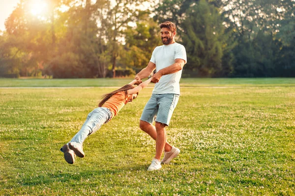 快乐的年轻父亲牵着他的小女儿 在一个温暖的阳光灿烂的日子里 在公园的草地上玩耍和玩乐 在一天的假期里一起玩得很开心 — 图库照片