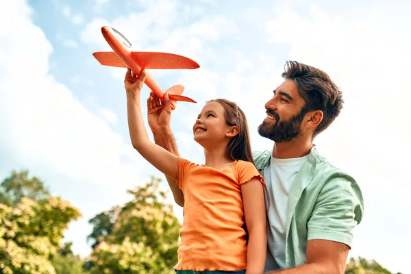 Young happy father playing with his daughter with an airplane in a meadow in the park on a warm sunny weekend.