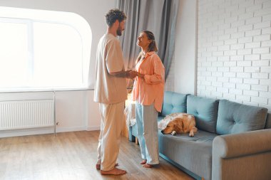 Birbirine aşık genç bir çift, sıcak bir evde oturma odasında duruyor ve sarılıyorlar, romantik bir şekilde birlikte vakit geçiriyorlar..