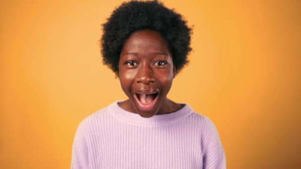 カーリーヘアのアフリカ系アメリカ人女性がショックで口を開き オレンジ色の背景から隔離された驚きの感情を示します — ストック動画