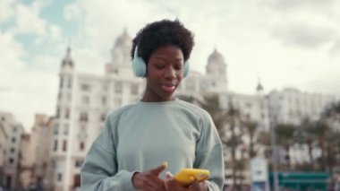 Afro saç stili kulaklıkla müzik dinleyen ve hafta sonu eğlenirken sokakta dans eden Afrikalı Amerikalı bir kadın..