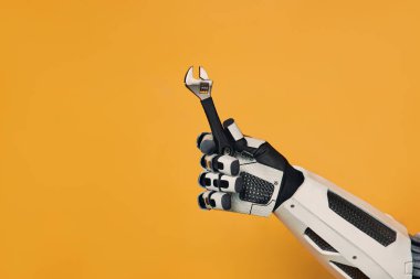 Robot, elinde turuncu bir arka planda izole edilmiş ayarlanabilir bir anahtar tutuyor. Robot ustası kavramı. İnsanlar ve yapay zeka arasındaki işbirliği.