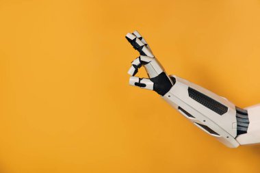 Robot el, turuncu arka planda izole bir hareket gösteriyor. İnsanlar ve yapay zeka arasındaki işbirliği.