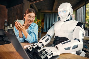 Bir fincan kahvesi olan genç bir kadın ve modern bir ofiste dizüstü bilgisayarın başında çalışan insansı bir robot. İnsanlar ve yapay zeka arasındaki işbirliği.