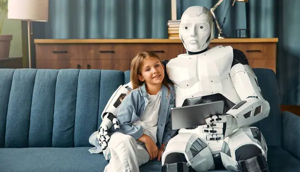 Robot housekeeper nurse using tablet with child girl sitting on sofa in living room. Collaboration between humans and artificial intelligence.