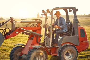 Olgun bir erkek çiftçi sıcak bir günde bir tarlada bir traktörde oturup çiftlikte çalışıyor. Çiftçilik ve tarım kavramı.