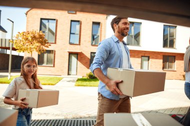 Genç evli bir çift ve kızları arabadan kutularca eşya indirip yeni bir eve taşıyorlar. Kiralamak ve bir ev almak. Taşınma konsepti.