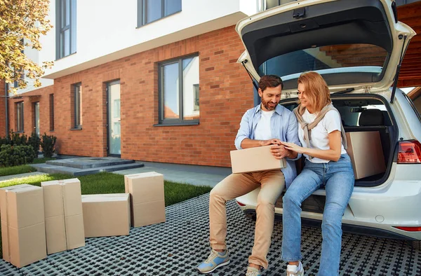 Genç evli bir çift bir arabanın bagajında oturuyor ve yeni evlerine bavullarını kutulara dolduruyorlar. Kiralamak ve bir ev almak. Taşınma konsepti.