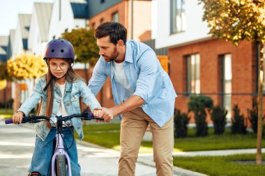 Mutlu bir baba küçük kızına bisiklet sürmeyi öğretti. Bir çocuk bisiklet sürmeyi öğrenir. Yazın aile aktiviteleri.