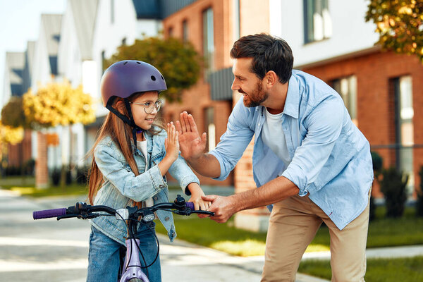 A happy father taught his little daughter to ride a bicycle. A child learns to ride a bicycle. Family activities in summer.