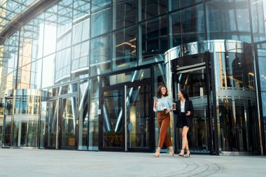 Çok ırklı başarılı iş kadınlarından oluşan bir ekip, ofise doğru yol alırken stratejiden, kahve içmekten ve telefon kullanmaktan bahsediyorlar. Arka planda binalar olan çeşitli kadınlar dışarıda yürüyor..
