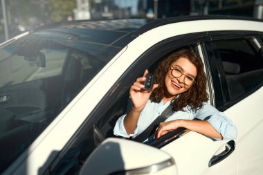 Yeni arabasında oturan güzel beyaz iş kadınının portresi ve anahtarları göstermesi. Bir araba alıp kiralamak. Seyahat, turizm, eğlence..