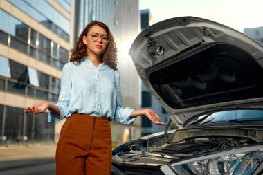 Yoldaki arabayla ilgili bir sorun var. Kaputu patlamış bir arabanın yanında duran kadın sürücü. Araç Sigortası, Bakım ve Servis Konsepti.