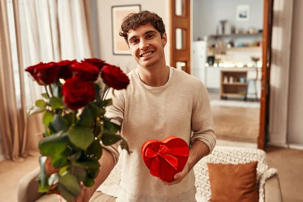 ハッピーバレンタインデー 赤いバラの花束と自宅のリビングルームで最愛の女性のためのハート型のギフトボックスを持つ男 — ストック写真