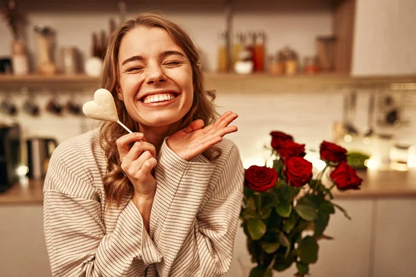 ハッピーバレンタインデー ハート型のチョコレートを食べている若い幸せな女性が自宅のキッチンのテーブルに座り 近くに立っている赤いバラの花束で — ストック写真