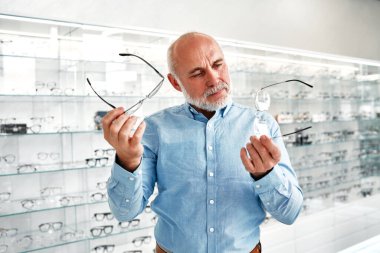 Yetişkin bir adam profesyonel bir mağazada kendine optik gözlük seçiyor. Görüş düzeltme ve göz doktorluğu.