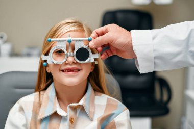 Göz testi yapan tatlı bir kız çocuğu optik dükkanındaki optometriste muayene oluyor. Göz doktoru klinikteki çocuk hasta için görüş testi yapıyor. Oftalmoloji ve göz düzeltmesi.