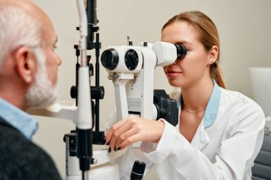 Optometriste ya da göz doktorunda doktora danışan olgun erkeklerin göz muayenesi. Optisyen hekimin yardımıyla ya da göz bebeği ya da retina görme sağlığıyla üst düzey müşteri test görüşünün yüzü.