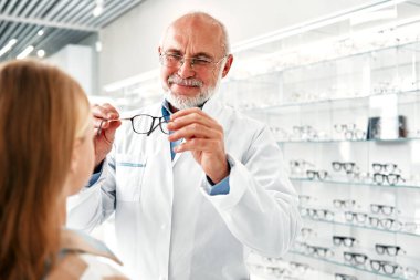 Olgun göz doktoru, çocuk bir kıza çeşitli gözlüklerle profesyonel bir mağazayı ziyaret ederken optik gözlük takar. Görme düzeltmesi. Sağlık, görme sorunu..