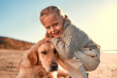 Tatlı küçük kız çocuğu dışarıda Golden Retriever köpeğiyle oynuyor. Kumsalda köpeği olan bir kız..