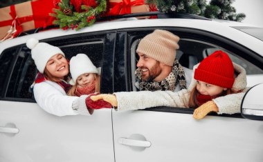 Mutlu Noeller ve mutlu yıllar. Kutular dolusu hediyelerle dolu bir arabada oturan mutlu bir aile ve karlı havada bir ormanın arka planında bir Noel ağacı..