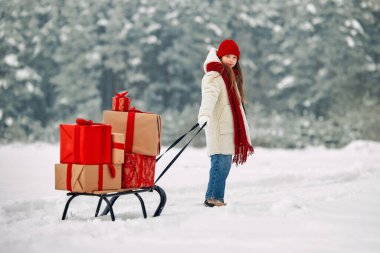 Mutlu Noeller ve mutlu yıllar. Tatlı bir kız, ormanın arka planında karlı bir yolda yürürken içinde hediyeler olan bir sürü kutu taşıyor..