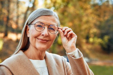 Güz mevsiminde parkta yürüyen gri saçlı, güzel, olgun bir kadın..