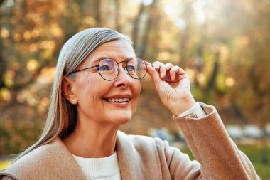 Güz mevsiminde parkta yürüyen gri saçlı, güzel, olgun bir kadın..