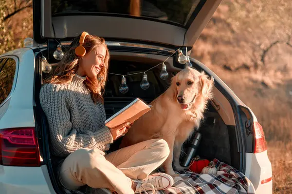 Szczęśliwa Kobieta Siedząca Bagażniku Samochodu Psem Ciepłym Kocu Słuchająca Muzyki — Zdjęcie stockowe