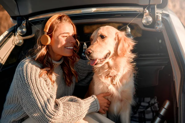 Szczęśliwa Kobieta Siedząca Bagażniku Samochodu Psem Ciepłym Kocu Słuchająca Muzyki — Zdjęcie stockowe