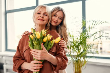 Anneler ve kadınlar günün kutlu olsun. Pencerenin yanındaki oturma odasında bir buket lale ile büyüleyici bir anne ve kız. Annenin sevgisi ve bakımı.