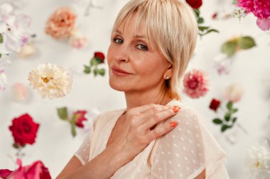 Anneler ve kadınlar günün kutlu olsun. Beyaz bir arka planda soyutlanmış, havada süzülen birçok çiçeğin etrafında, beyaz elbiseli, çekici, olgun bir kadın..