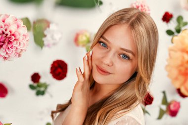 Mutlu Kadınlar Günü. Beyaz bir arka planda izole edilmiş narin elbiseli çekici genç bir kadın havada süzülen birçok çiçeğin etrafında..