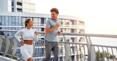 Spor giyimli bir çift köprüde dışarıda koşuyor. Sabah egzersizleri ve koşu. Spor ve eğlence, aktif yaşam tarzı.