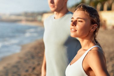 Spor giyimli bir çift deniz kıyısında ısınma egzersizi yapıyor. Sabah egzersizleri ve koşu. Spor ve eğlence, aktif yaşam tarzı.