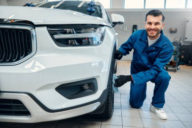 Araba temizliği. Adam mikrofiberi elinde tutuyor ve arabayı cilalıyor. Araba yıkamada araba lastiklerini yıkayan işçi mikrofiber bezle araba temizleyen adam, araba temizleme konsepti..