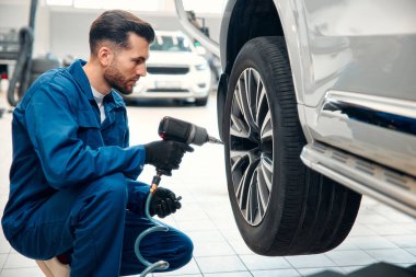 Tamirci garajda çalışıyor ve tekerlek alaşımı değiştiriyor. Tamir ya da bakım servisi. Tamirhanede lastik tutan tamirci. Kış ve yaz lastiklerinin yenisi..
