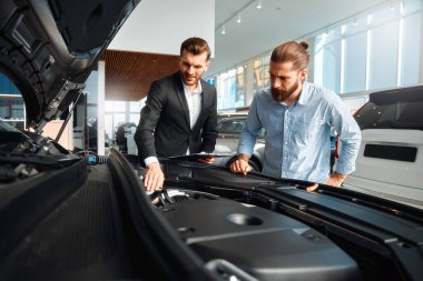Satıcı veya araba satıcısı ve müşteri veya müşteri showroom yeni ve ikinci el araçların motor performansını sunan araba bayilik, erkek kaputun altında bakan