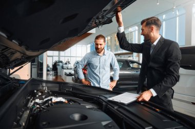 Satıcı veya araba satıcısı ve müşteri veya müşteri showroom yeni ve ikinci el araçların motor performansını sunan araba bayilik, erkek kaputun altında bakan