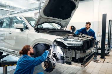 İki servis teknisyeni teşhis sonuçlarını aldıktan sonra arabayı inceliyor. Onarım servisi kavramı.