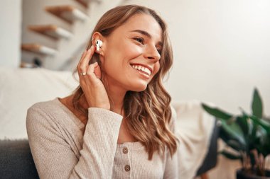 Evde oturma odasındaki kanepenin yanında otururken müzik ya da kulaklık dersi alan genç bir kadın..