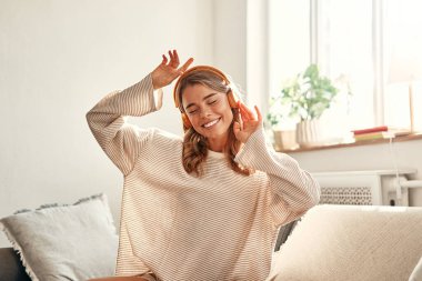 Evde oturma odasındaki kanepenin yanında otururken müzik ya da kulaklık dersi alan genç bir kadın..