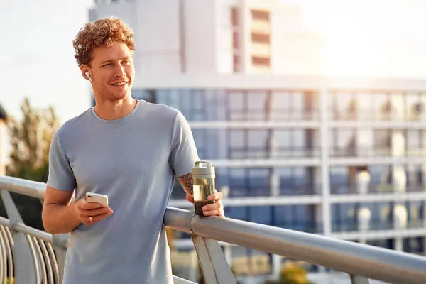 Man Drinks Water Uses Smartphone While Resting Running Outdoors Bridge — Stock Photo, Image
