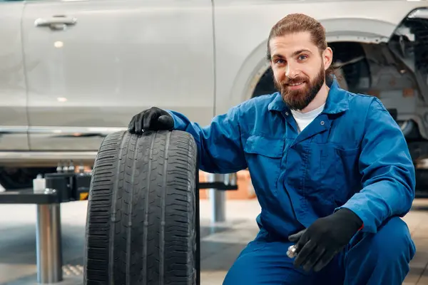 Car mechanic working in garage and changing wheel alloy tire. Repair or maintenance auto service. Mechanic holding a tire tire at the repair garage, replacement of winter and summer tires.