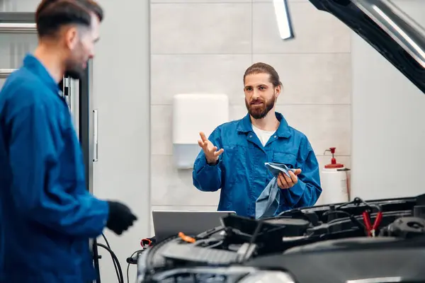 Two mechanics are repairing a car in a workshop. Auto mechanic detailed inspection of the car. Auto car repair service center. Car service, repair, maintenance concept.
