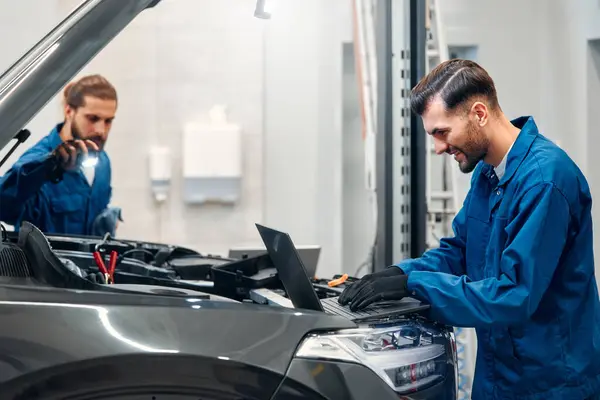 Two mechanics are repairing a car in a workshop. Auto mechanic detailed inspection of the car. Auto car repair service center. Car service, repair, maintenance concept.